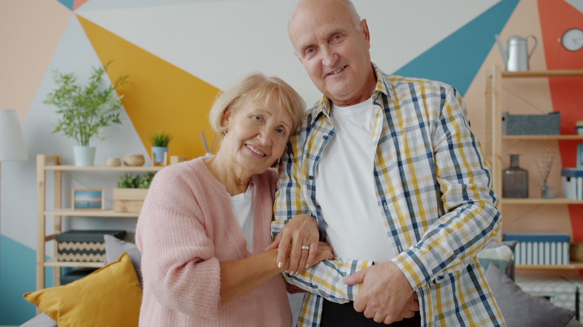 An older couple smiling together at home in a bright, plant-filled room