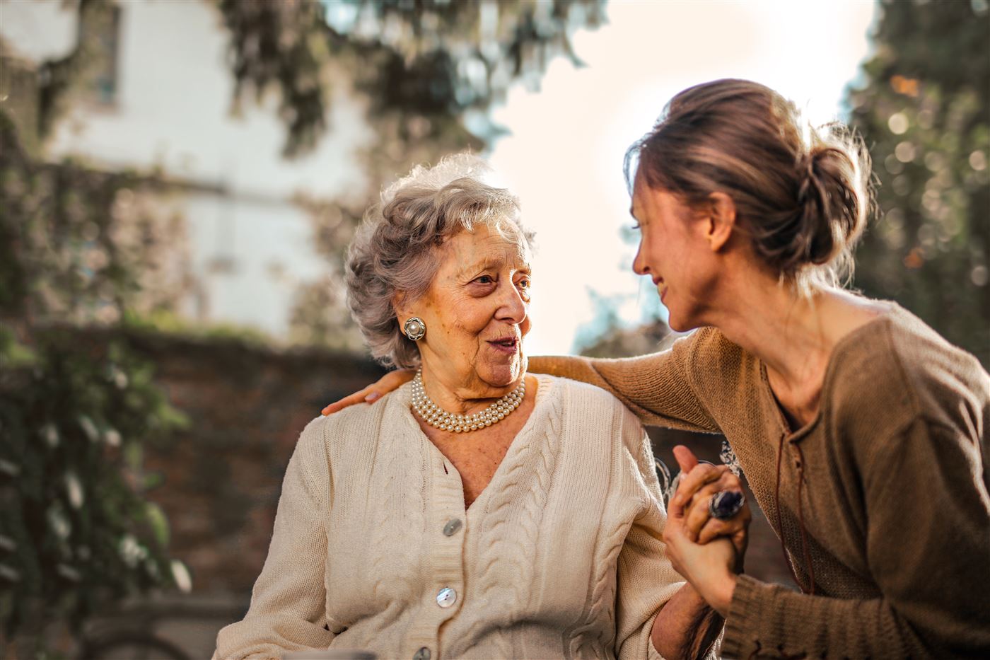 An adult daughter and her senior mother sharing a joyful moment in a sunlit garden